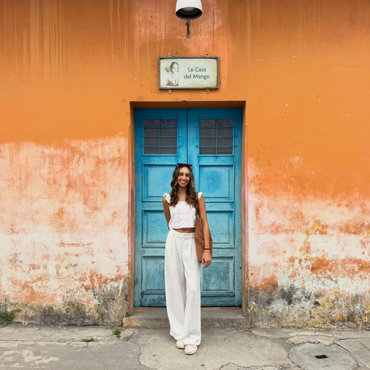 Natasha in white in front of an orange wall and a blue door, Antigua